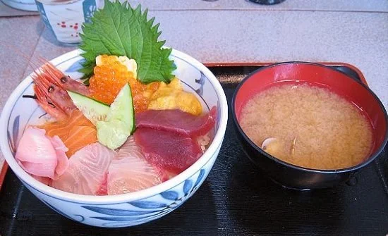 海鮮丼旁放著味噌湯,丼飯上有生魚片、海膽與鮭魚卵。