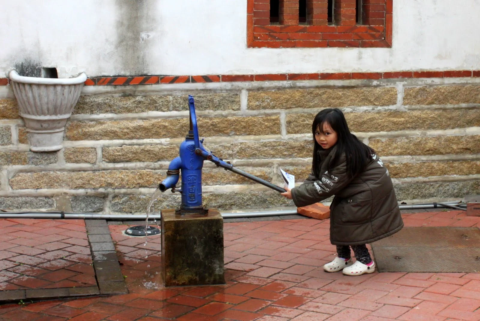 小女孩操作藍色汲水幫浦，清水流向地面